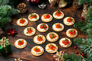 Salmon caviar and soft cheese savory crackers with decoration, gifts, green tree branch on wooden rustic table.
