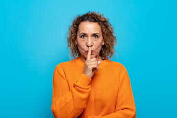 middle age woman looking serious and cross with finger pressed to lips demanding silence or quiet,...