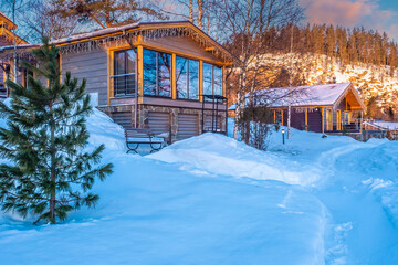 Cottage village in winter. Houses at the bottom of the hill. Paths in the snow lead to the cottages. House with panoramic Windows on the background of snow. Early evening in the countryside.