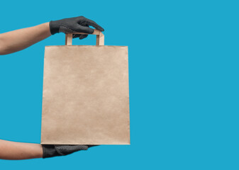Empty paper bag. Shopping bag for groceries. Hands in black gloves. On a blue background.