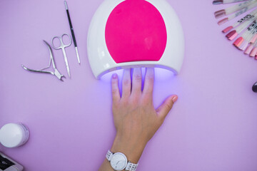 Women's hands dry gel Polish in an ultraviolet lamp, top view on the table in the salon of gel manicure. the process of drying the gel on the nails. modern manicure technology. Professional manicure 