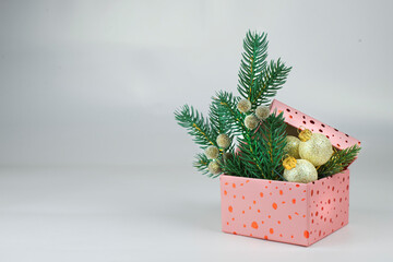 pink box with golden christmas balls and green branches of christmas tree