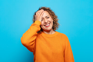 middle age woman laughing and slapping forehead like saying d’oh! I forgot or that was a stupid...