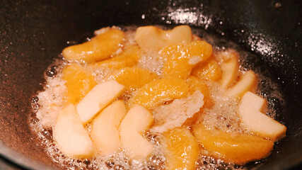 Apple and orange are fried in a pan in a sugar sauce
