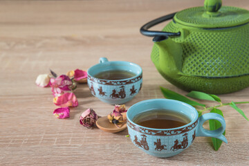 Tea time concept. Chinese iron tea pot, two cups, rose buds, bamboo stem on wooden table. Close up, selective focus
