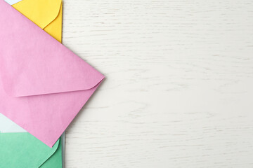 Colorful paper envelopes on white wooden background, flat lay. Space for text