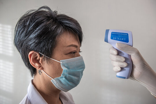 Hand holding infrared thermometer to measuring temperature on Asia woman with face mask with white background. Covid19 screening and new normal concept