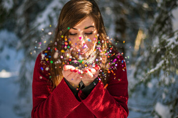 Christmas special portrait of an European woman blowing colourful objects in a winterland