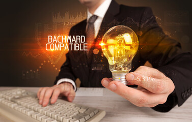 Businessman holding lightbulb with BACKWARD COMPATIBLE inscription, Business technology concept