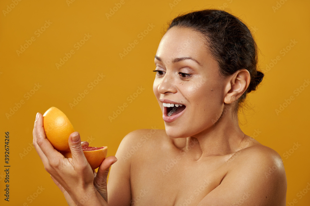 Wall mural portrait of a young woman african-american on a yellow background. a woman steals half of a grapefru