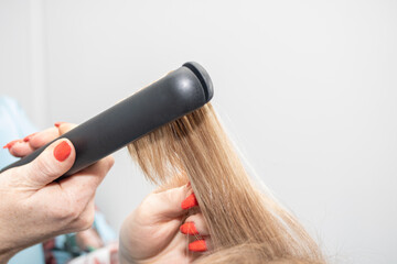 Barber straightens long hair with a hair iron, close-up.