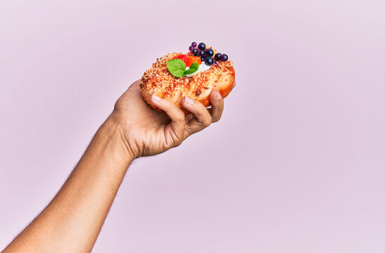 Hand of hispanic man holding sweet bun over isolated pink background.