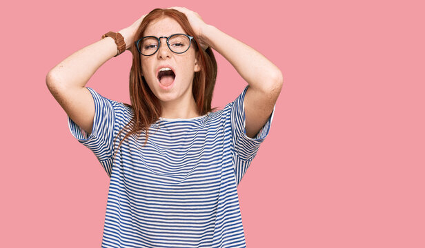 Young read head woman wearing casual clothes and glasses crazy and scared with hands on head, afraid and surprised of shock with open mouth