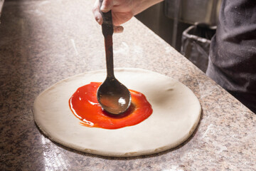 male chef smears tomato sauce on the base of the pizza. ketchup on pizza