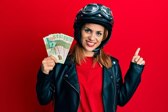 Hispanic young woman wearing motorcycle helmet holding hong kong dollars smiling happy pointing with hand and finger to the side