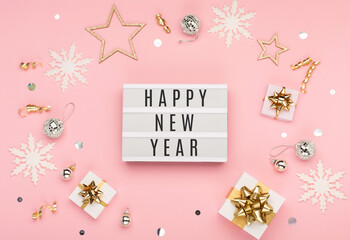 Happy New Year text on white Lightbox with gift boxes, holiday silver and gold decorations, snowflakes on pink paper background.