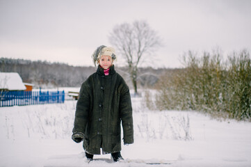 Fototapeta na wymiar Emotional portrait of positive slavonic girl wearing loose fit padded jacket with scarf on her head in winter snowy day in village
