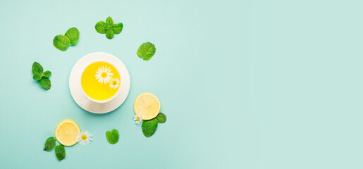 Lemon and mint tea with chamomile flower on blue paper background.