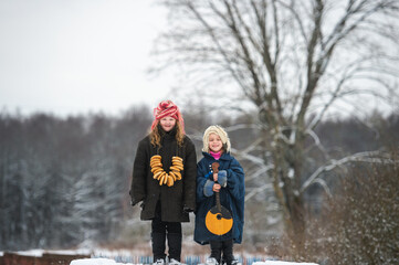 Two beautiful village girls stand on the bench with balalaika and barankas in winter with mum