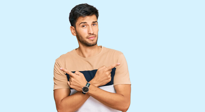 Young handsome man wearing casual clothes pointing to both sides with fingers, different direction disagree