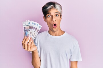 Young hispanic man holding russian 500 ruble banknotes scared and amazed with open mouth for...