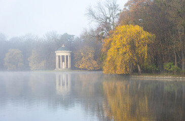 Fototapeta na wymiar Herbstspaziergang im Schlosspark in München - See und Monopteros im morgendlichen Nebel