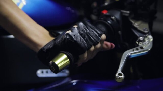 A woman's hand in a leather glove squeezes the clutch and turns the throttle grip of a sports motorcycle