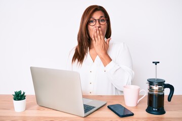 Middle age brunette hispanic business woman working at the office covering mouth with hand, shocked and afraid for mistake. surprised expression