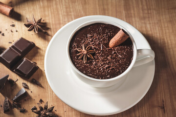 Hot chocolate drink in white cup, broken chocolate, cinnamon stick and star anise on a wooden table