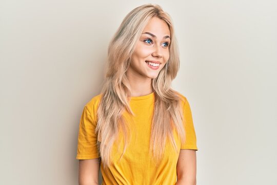 Beautiful caucasian blonde girl wearing casual tshirt looking away to side with smile on face, natural expression. laughing confident.