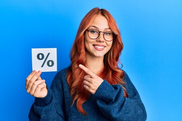 Young beautiful redhead woman holding percentage symbol smiling happy pointing with hand and finger