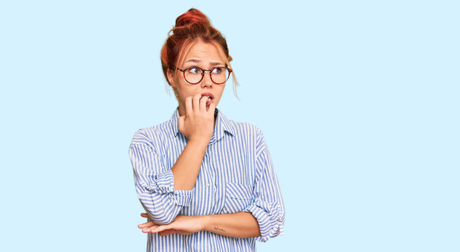 Young redhead woman wearing casual clothes and glasses looking stressed and nervous with hands on mouth biting nails. anxiety problem.
