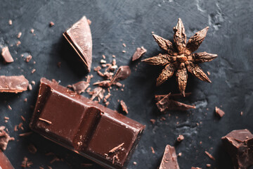 Broken chocolate cubes and star anise on dark textured background, top view