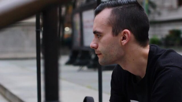 Young man sitting on the steps smoking a green vape pen looking ahead