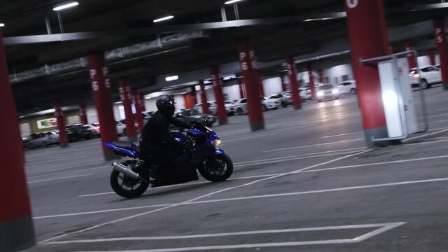 Motorcyclist in black clothes and helmet drives blue sports bike in an underground parking lot at night