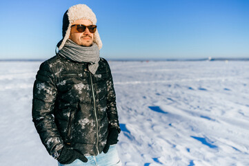 Fototapeta na wymiar Dreaming stylish man in sunglasses posing in the snow field