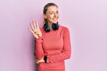 Beautiful caucasian woman wearing sportswear and arm band showing and pointing up with fingers number four while smiling confident and happy.