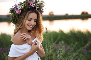 Fototapeta premium Young woman wearing wreath made of beautiful flowers outdoors at sunset