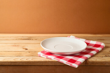 Empty plate with checked tablecloth on wooden table. Kitchen or restaurant background