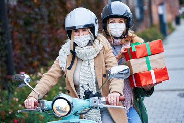 Two women wearing masks and holding shopping bags on scooter
