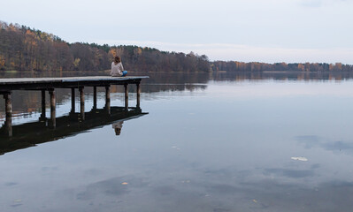 Attractive young female sitting at the edge of a pier while enjoying the views of a lake in Trakai, Lithuania. This city was the ancient capital of this baltic republic.