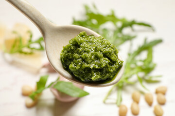 Spoon of tasty arugula pesto on blurred background, closeup
