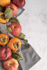 Seasonal ripe fruits - red apple and persimmons on grey background, space for text
