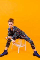 Stylish young girl posing on stepladder over orange background