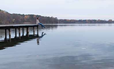 Attractive young female sitting at the edge of a pier while enjoying the views of a lake in Trakai, Lithuania. This city was the ancient capital of this baltic republic.