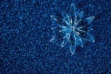 Simple winter or Christmas concept: crystal ornament - snowflake on dark blue glitter background, selective focus, free copy space