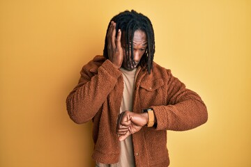 African american man with braids wearing brown retro jacket looking at the watch time worried,...
