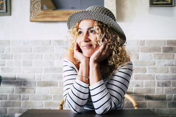 portrait of beautiful curly woman at the table of restaurant thinking and dreaming looking away smiling