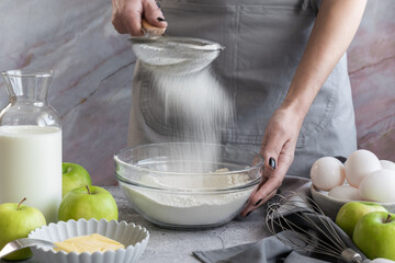 Woman sifting flour through sieve, preparing homemade sweet pie with ripe apples - Powered by Adobe