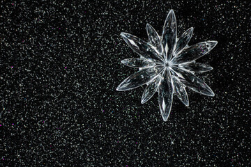Simple winter or Christmas concept: crystal ornament - snowflake on black glitter background, selective focus, free copy space
